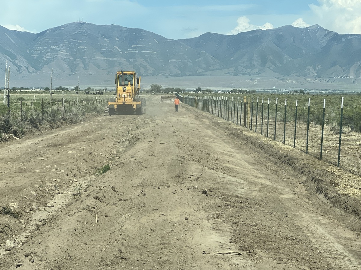 Road building with grader and crew, mountain backdrop