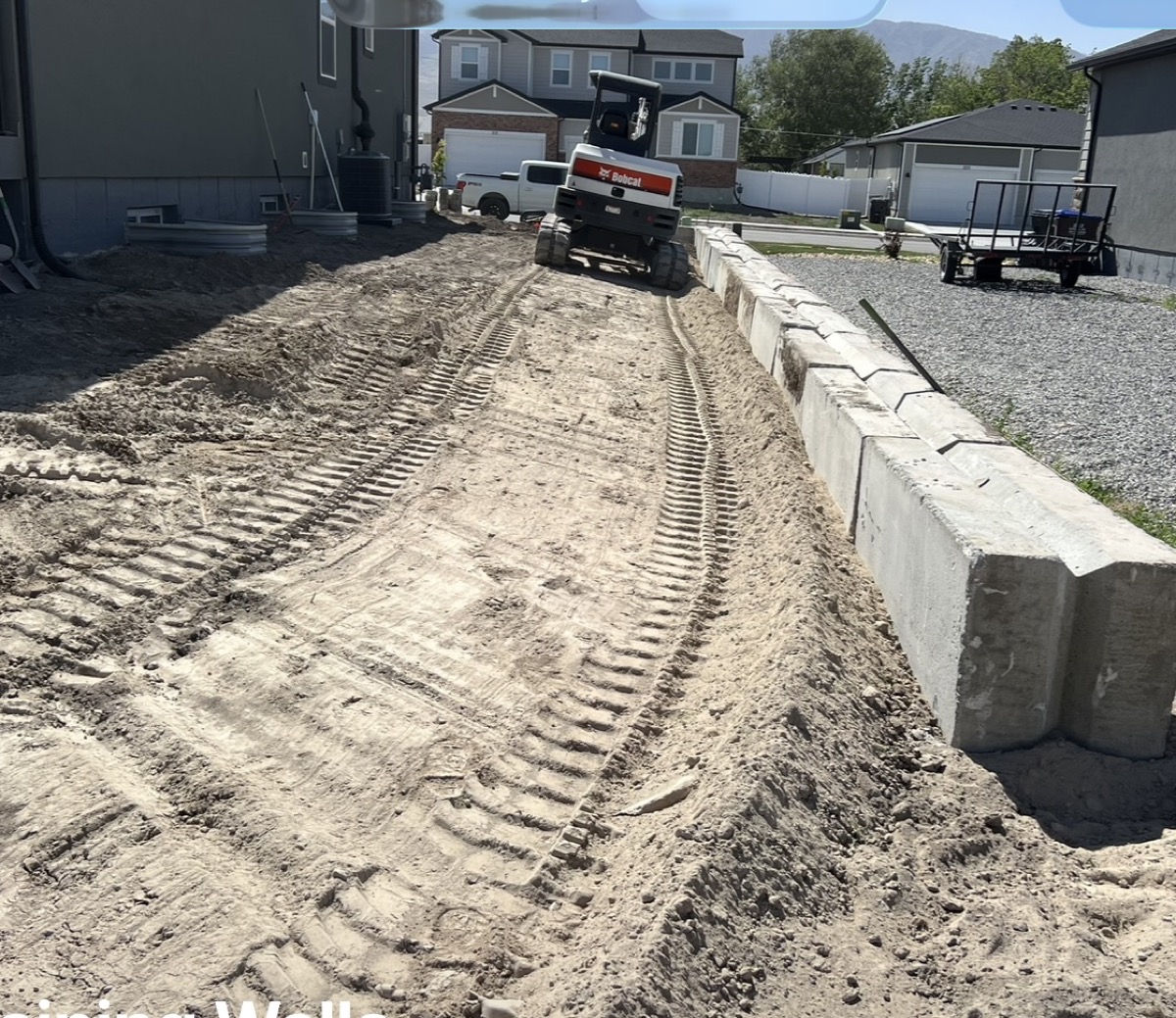 Concrete block retaining wall under construction with Bobcat