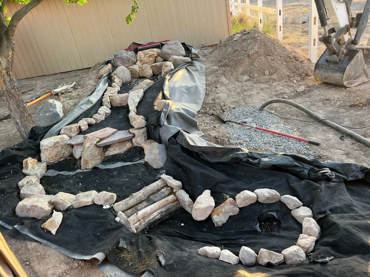 Water feature pond under construction with liner, boulders, and rock surround